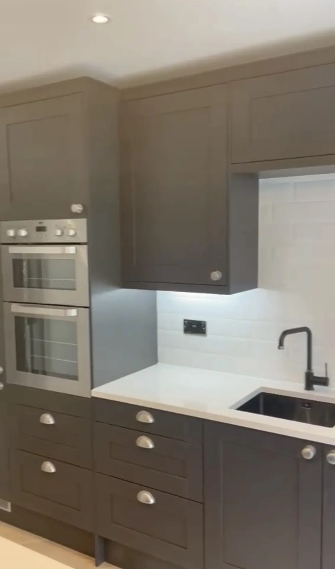 Recent fitted kitchen with dark cabinetry, white worktop and built-in double oven